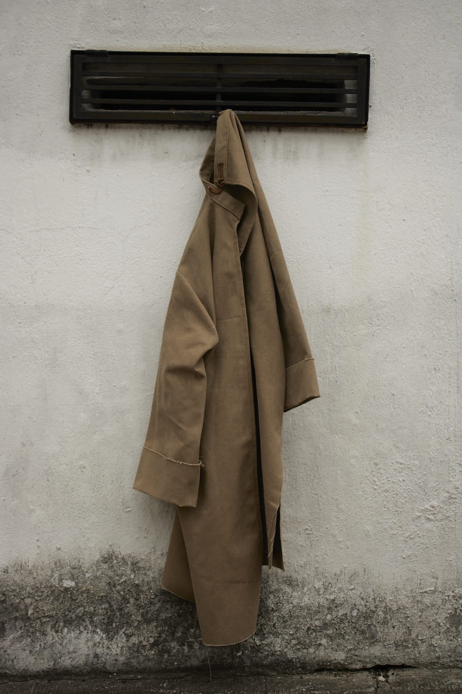 The FRAME coat hanging on a hook beneath a vent on a white wall