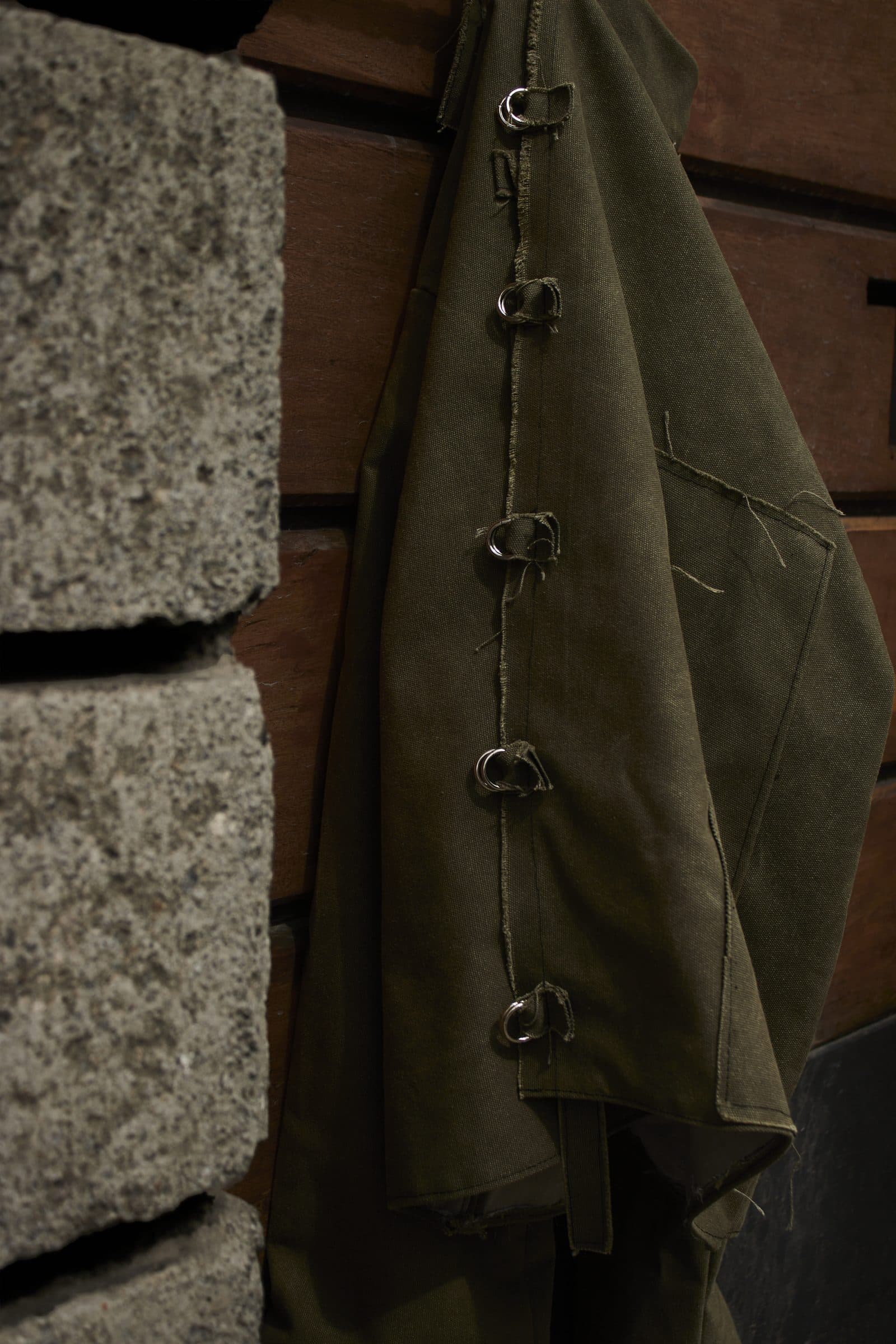 The AKIN jacket hanging against stone and wood