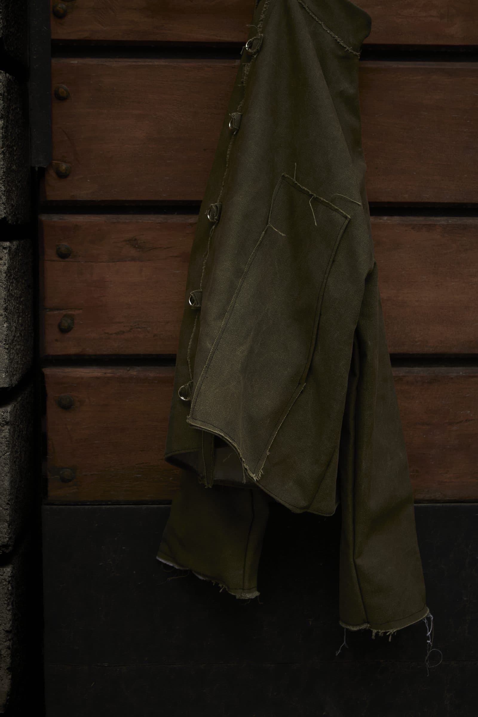 Detail of the AKIN jacket hanging, with raw hem and metal rings