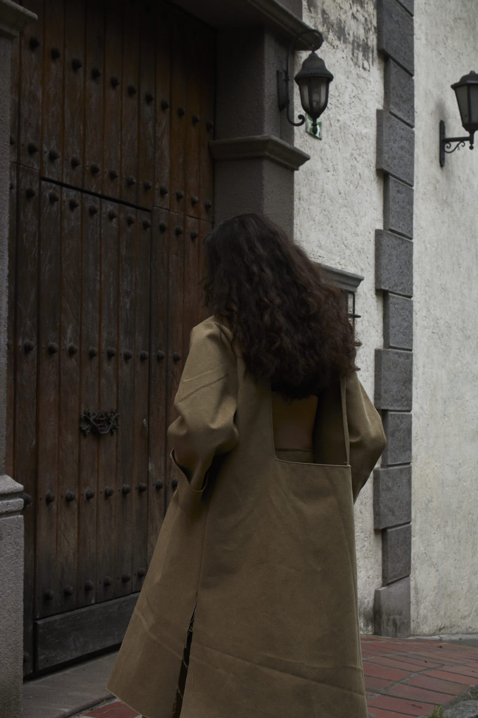 The FRAME coat from behind, worn in front of a dark wooden door