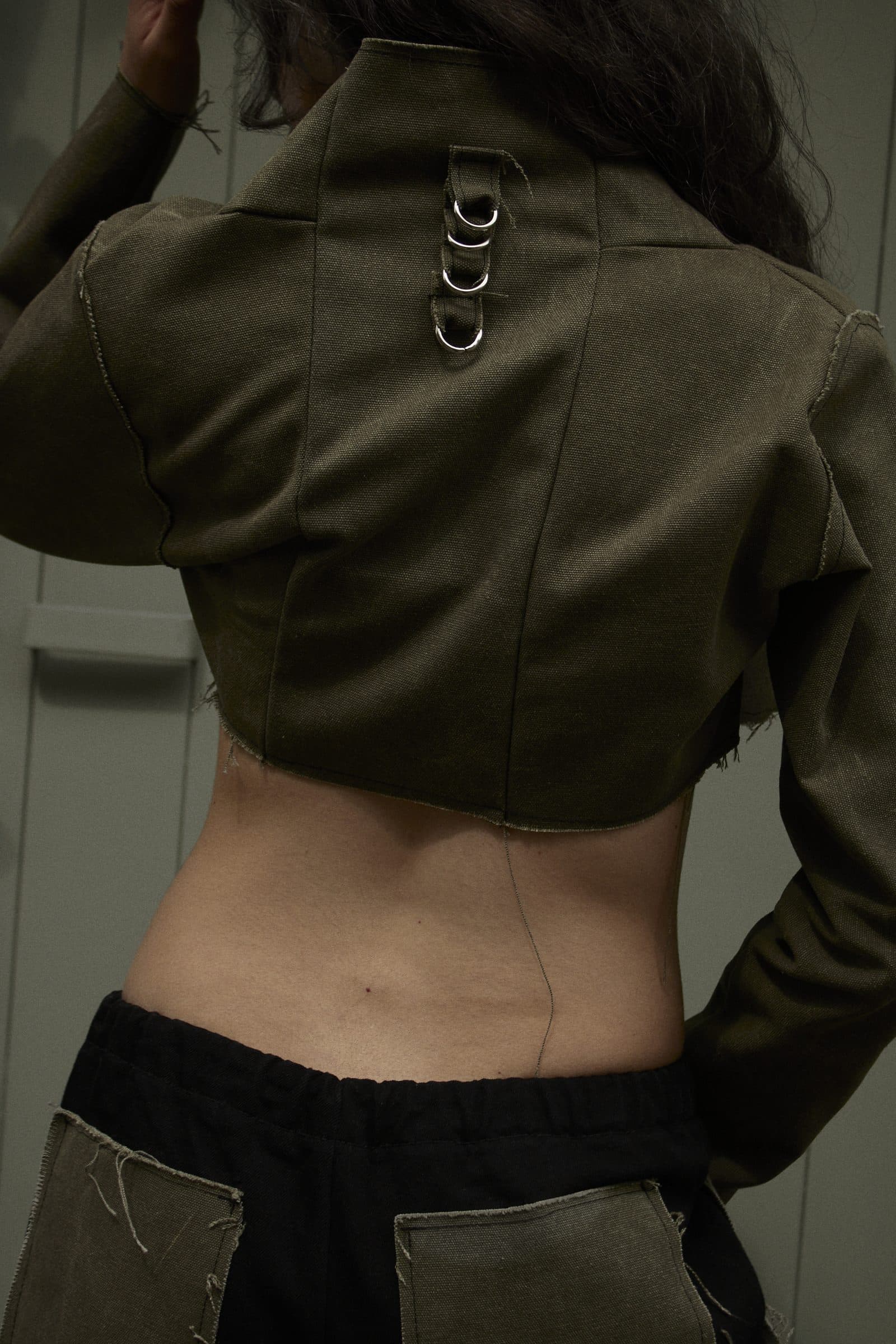 SAGE cropped jacket, seen from behind, with three metal rings at the collar